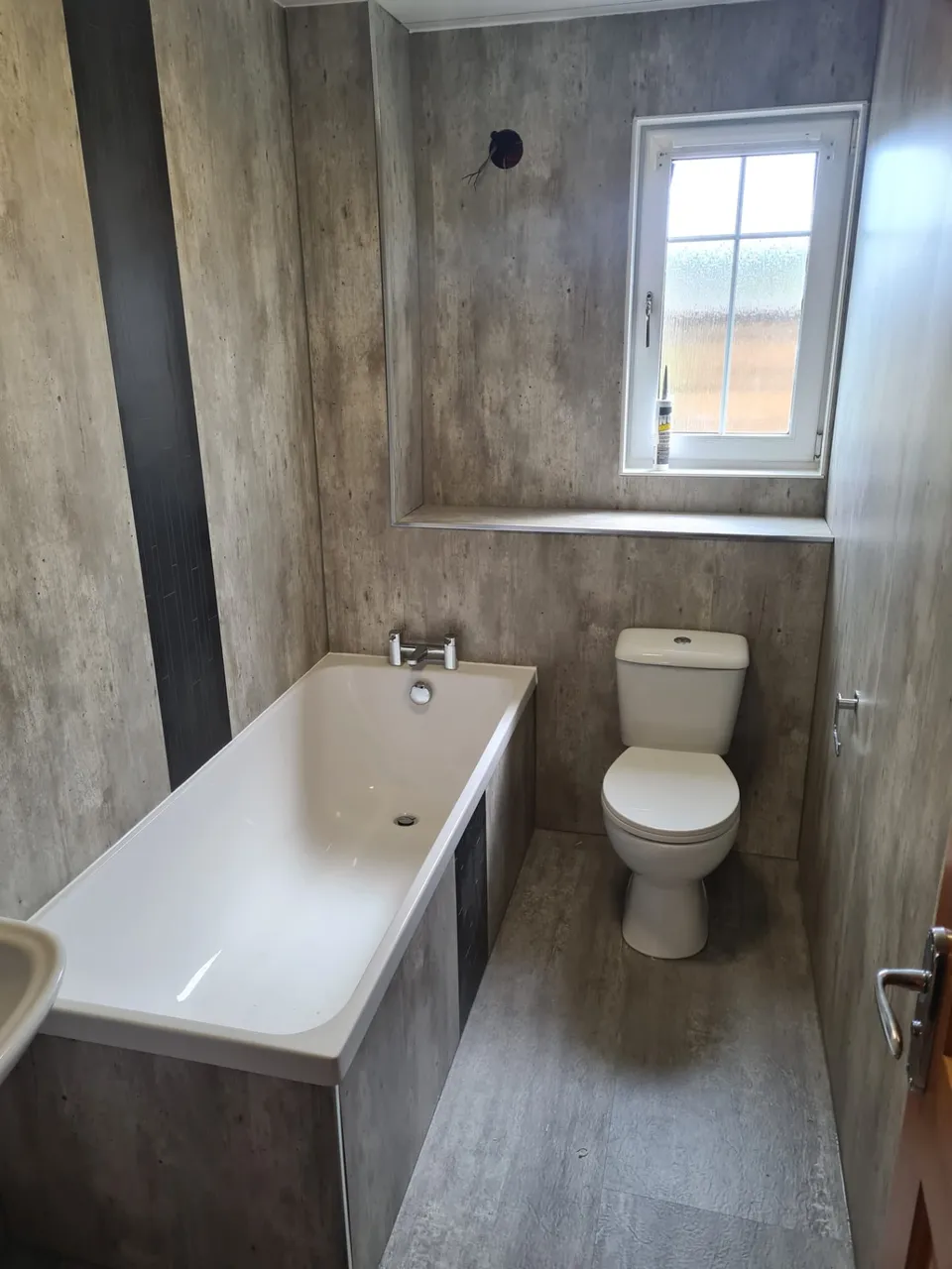 Bathroom refit with concrete-effect wall panels, white bath and close-coupled toilet