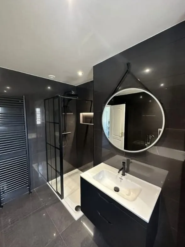 Modern bathroom installation with black grid shower screen, black heated towel rail and floating vanity unit