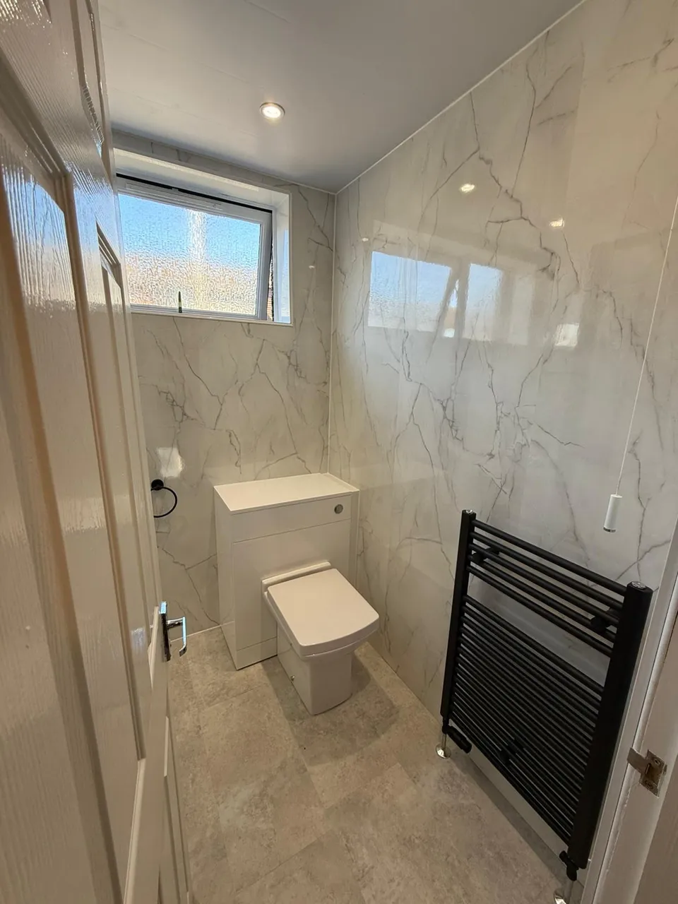 Cloakroom bathroom with marble-effect wall panels, back-to-wall toilet and black towel radiator