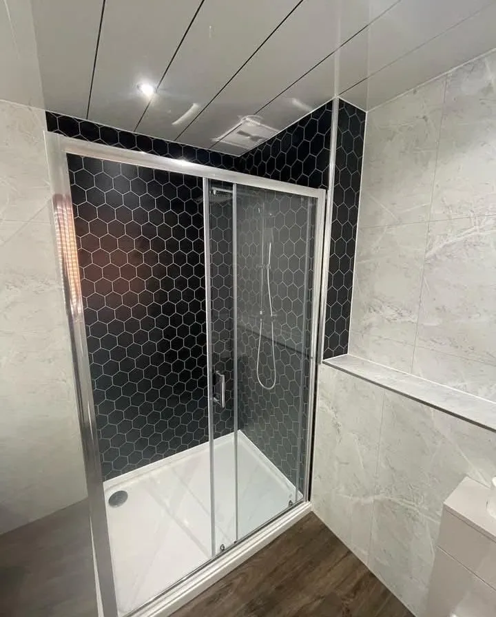 Sliding-door shower enclosure with black hexagon wall tiles and marble-effect panels