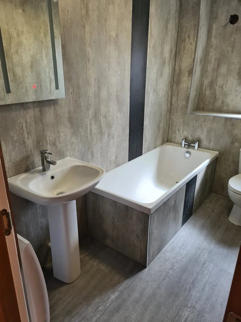 Bathroom with grey concrete-effect panels, pedestal basin and panelled bath