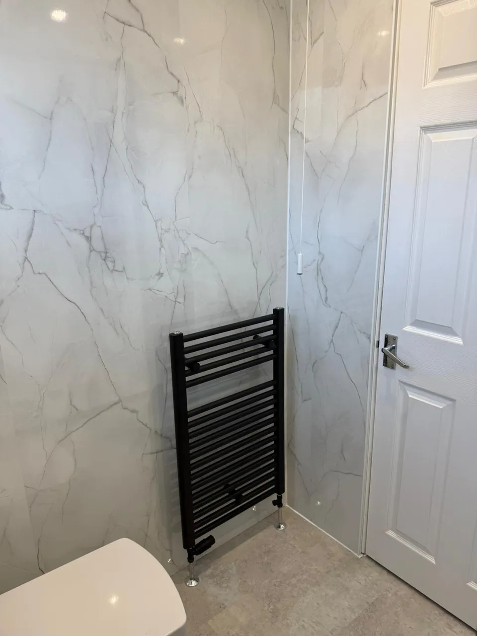 Central Heating & Radiators in Kirkcaldy and Fife: Black heated towel rail fitted against white marble-effect bathroom wall panels