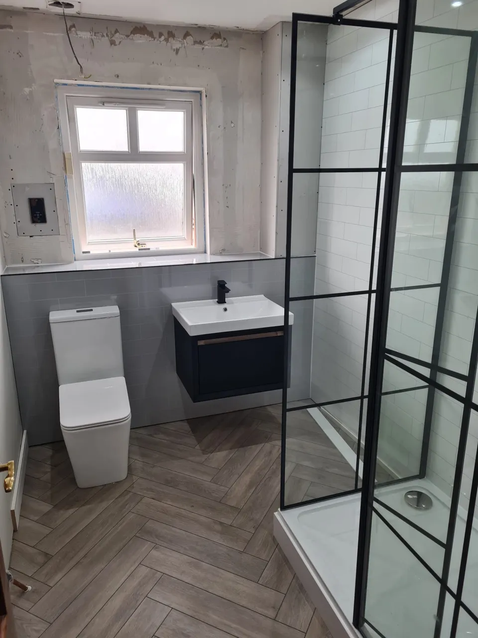 Bathroom installation in progress: herringbone floor, grid shower screen and wall-hung basin fitted